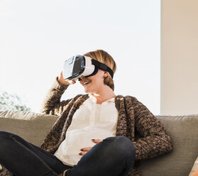 Schwangere Frau auf Couch mit VR-Brille - UUF09603