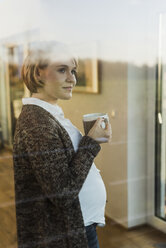 Pregnant woman behind windowpane holding a drink in mug - UUF09613