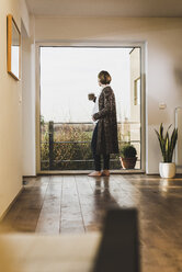 Pregnant woman standing at the window holding a mug - UUF09614