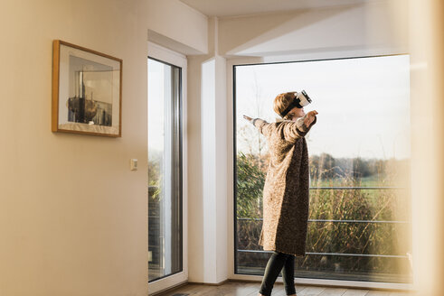 Schwangere Frau steht am Fenster und trägt eine VR-Brille - UUF09619