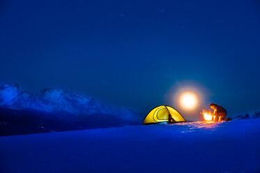 Senior man camping in snow-covered landscape at full moon - HHF05487