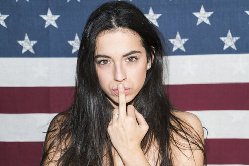 Junge Frau steht vor der US-Flagge und macht ein freches Handzeichen - KKAF00220