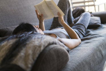 Junge Frau liegt auf der Couch und liest ein Buch - KKAF00224