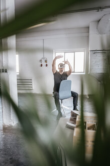 Mann sitzt auf einem Stuhl in einem leeren Loft und trägt eine VR-Brille - KNSF00819