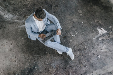 Businessman sitting on concrete floor using laptop - KNSF00829