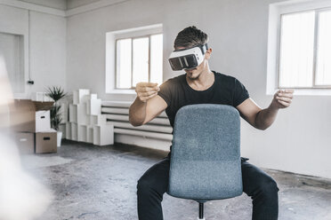 Mann sitzt auf einem Stuhl in einem leeren Loft und trägt eine VR-Brille - KNSF00842