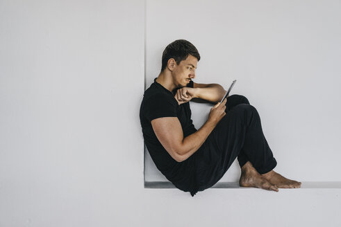 Mann sitzt in einer Nische und benutzt ein Tablet - KNSF00865