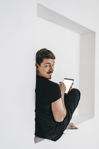 Mann sitzt in einer Nische und benutzt ein Tablet, lizenzfreies Stockfoto