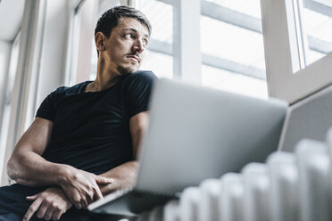 Man sitting on heater with laptop - KNSF00867