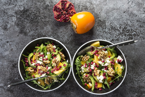 Two bowls of avocado salad with rocket, pomegranate seed, kaki, feta and walnuts stock photo