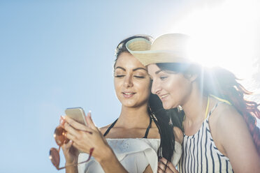 Zwei junge Frauen mit Mobiltelefon unter blauem Himmel - ZEF11999