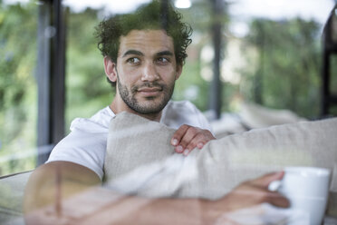 Young man drinking coffee sitting on couch - ZEF12013