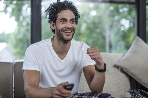 Happy young man sitting on couch watching tv stock photo
