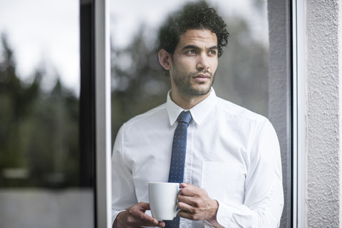 Businessman with cup of coffee looking out of window stock photo