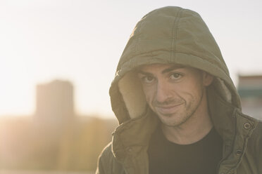 Portrait of smiling man wearing hooded jacket outdoors at sunset - SKCF00237