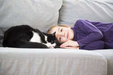 Portrait of little girl lying on couch with cat - LVF05773