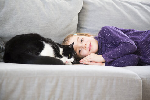 Porträt eines kleinen Mädchens, das mit einer Katze auf der Couch liegt - LVF05773