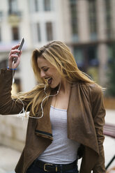 Glückliche junge Frau hört Musik mit Kopfhörern und Smartphone - KKAF00244