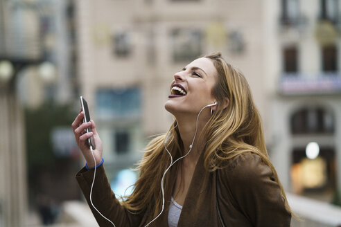 Glückliche junge Frau hört Musik mit Kopfhörern und Smartphone - KKAF00245