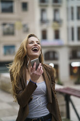 Glückliche junge Frau hört Musik mit Kopfhörern und Smartphone - KKAF00246