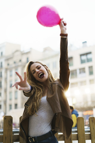 Porträt einer glücklichen jungen Frau mit Luftballon und Siegeszeichen, lizenzfreies Stockfoto