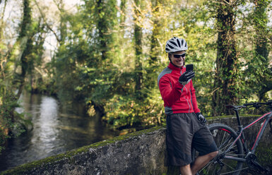 Mountainbiker fotografiert im Wald mit seinem Smartphone - RAEF01606