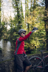 Mountainbiker fotografiert im Wald mit seinem Smartphone - RAEF01607