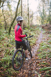 Junger Mann beim Mountainbiken im Wald - RAEF01616