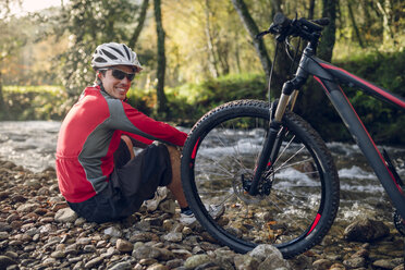 Mountain biker sitting at river - RAEF01622
