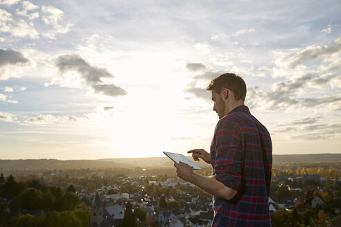 Man using tablet on a hill above a town - FMKF03374