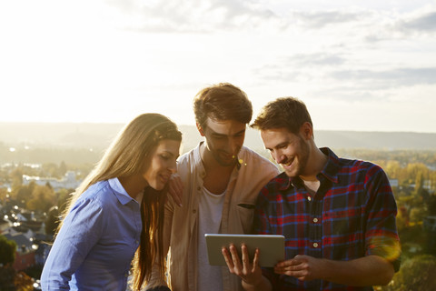 Glückliche Freunde teilen sich ein Tablet im Freien, lizenzfreies Stockfoto