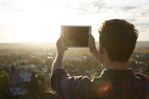 Mann fotografiert mit einem Tablet auf einem Hügel über einer Stadt, lizenzfreies Stockfoto