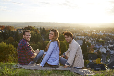 Glückliche Freunde sitzen auf einem Hügel über einer Stadt - FMKF03379