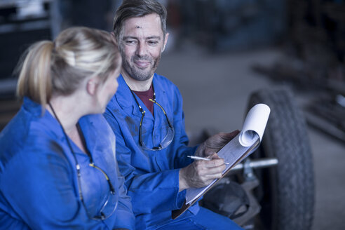 Mann und Frau in blauen Overalls in einer Werkstatt, Mann mit Klemmbrett - ZEF12126