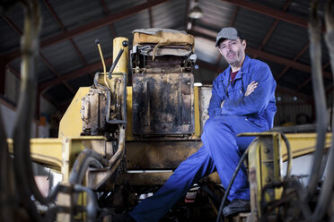 Mann in blauem Overall sitzt an einer Maschine in einer Werkstatt - ZEF12130