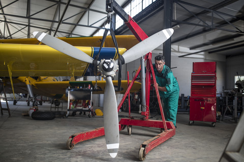 Mechaniker im Hangar beim Schieben des Propellers eines Leichtflugzeugs, lizenzfreies Stockfoto