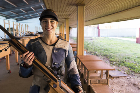 Porträt einer lächelnden Frau, die ihr Sportgewehr in einem Schießstand hält - ABZF01704