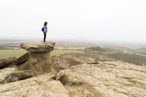 Spanien, Navarra, Bardenas Reales, junge Frau steht auf einem Felsen im Naturpark und betrachtet die Aussicht - KKAF00251