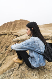 Spanien, Navarra, Bardenas Reales, junge Frau sitzt auf einem Felsen im Naturpark und betrachtet die Aussicht - KKAF00252