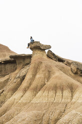 Spanien, Navarra, Bardenas Reales, junge Frau sitzt auf einem Felsen im Naturpark und betrachtet die Aussicht - KKAF00253