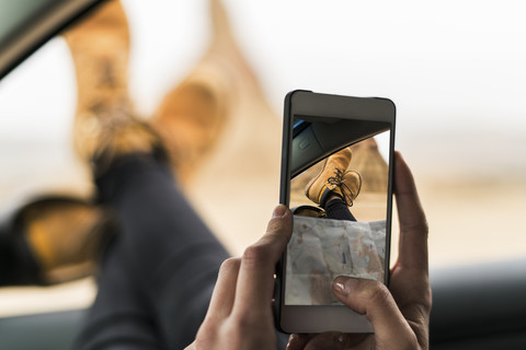 Spain, Navarra, Bardenas Reales, young woman with legs of leaning out of car window taking selfie stock photo