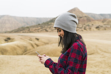 Spanien, Navarra, Bardenas Reales, lächelnde junge Frau, die im Naturpark auf ihr Handy schaut - KKAF00272