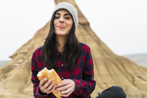 Spanien, Navarra, Bardenas Reales, Porträt einer lächelnden jungen Frau, die in einem Naturpark Baguette isst, lizenzfreies Stockfoto