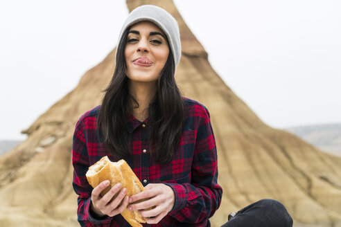 Spanien, Navarra, Bardenas Reales, Porträt einer lächelnden jungen Frau, die in einem Naturpark Baguette isst - KKAF00277