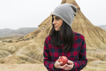 Spain, Navarra, Bardenas Reales, young woman with apple in nature park - KKAF00278