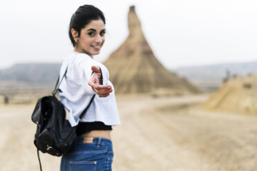 Spain, Navarra, Bardenas Reales, smiling young woman reaching out her hand to viewer - KKAF00286