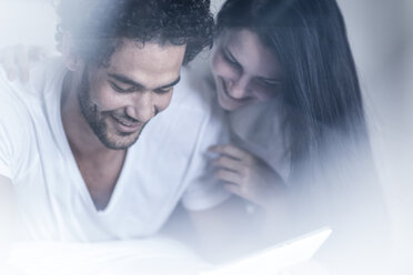 Lächelndes junges Paar im Bett mit Blick auf ein Tablet - ZEF12187