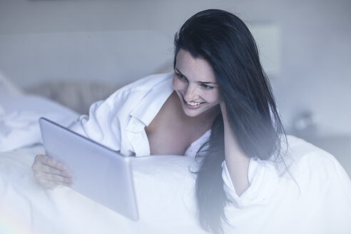 Lächelnde junge Frau im Bett mit Tablet - ZEF12194