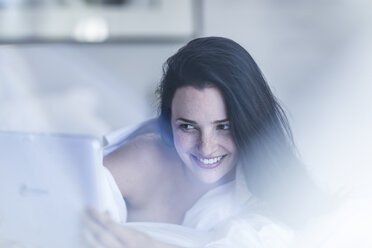 Smiling young woman lying in bed using tablet - ZEF12196