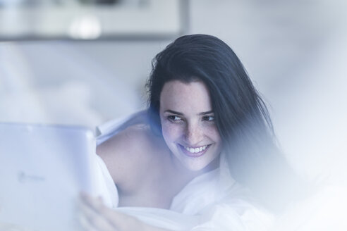 Lächelnde junge Frau im Bett liegend mit Tablet - ZEF12196